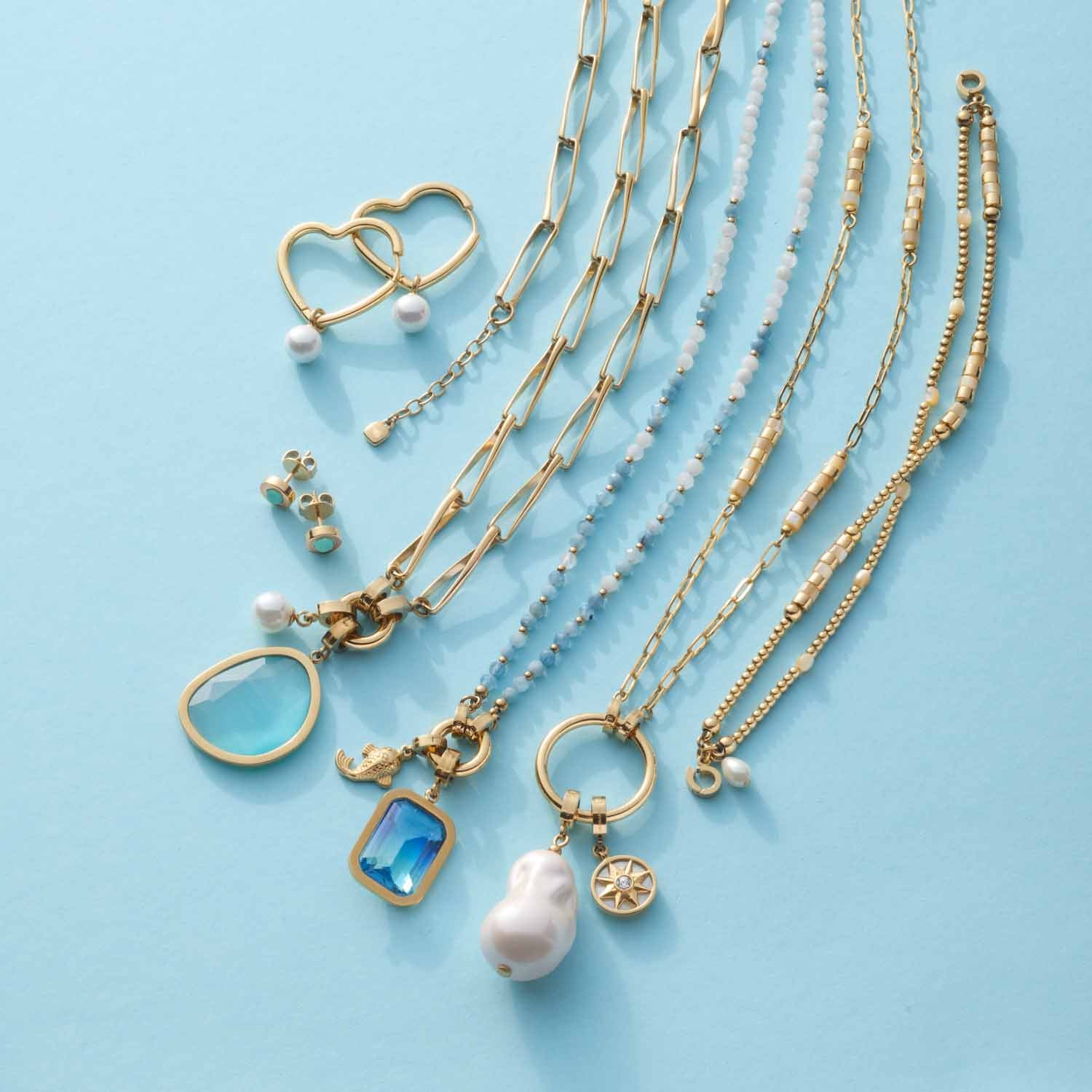 Creole LULU gold mit verschiedenen Halsketten und Schmuckzubehoer auf hellblauem Untergrund
