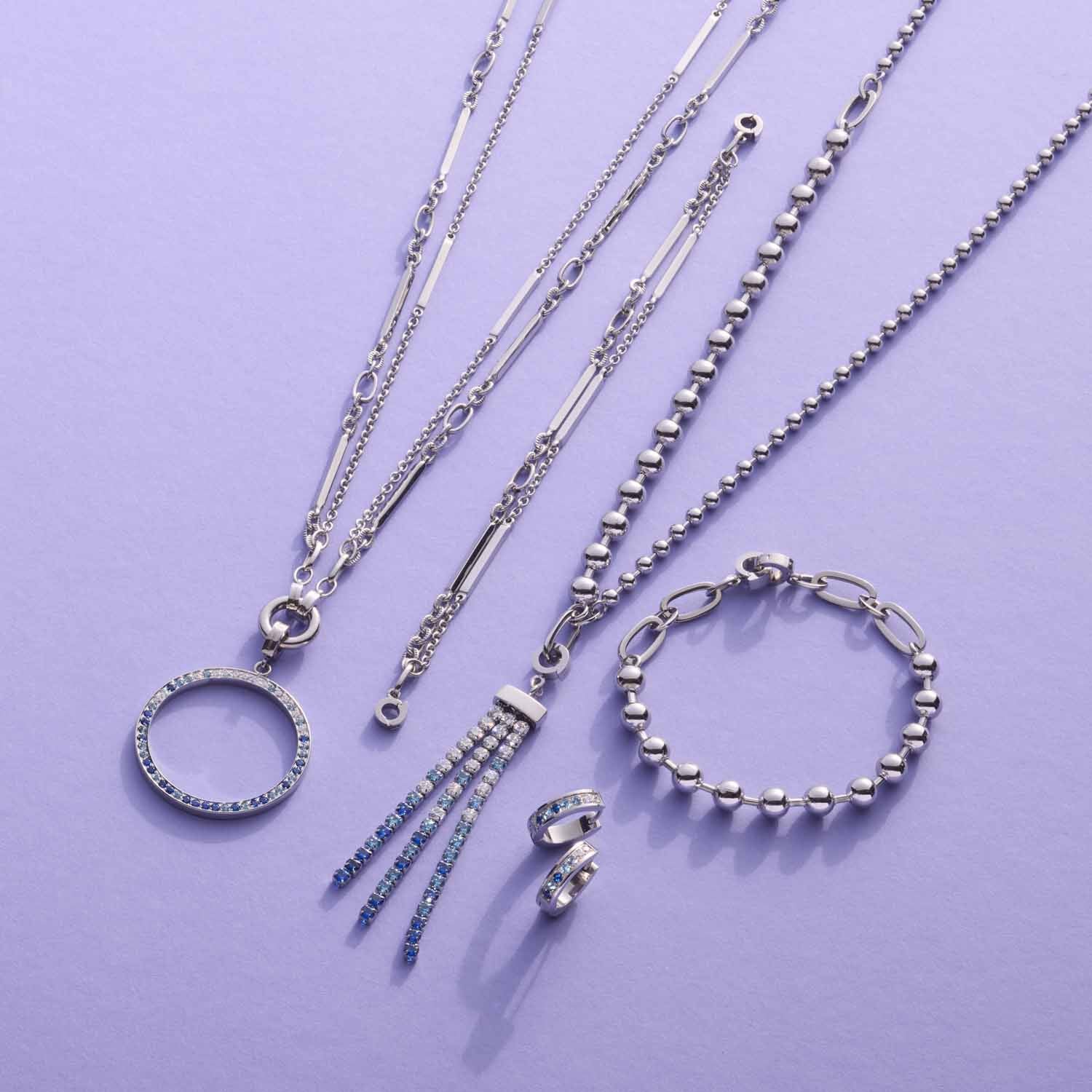 Schmuckkollektion aus Edelstahl: Halsketten, Creolen, Armband und Ohrringe auf violettem Hintergrund