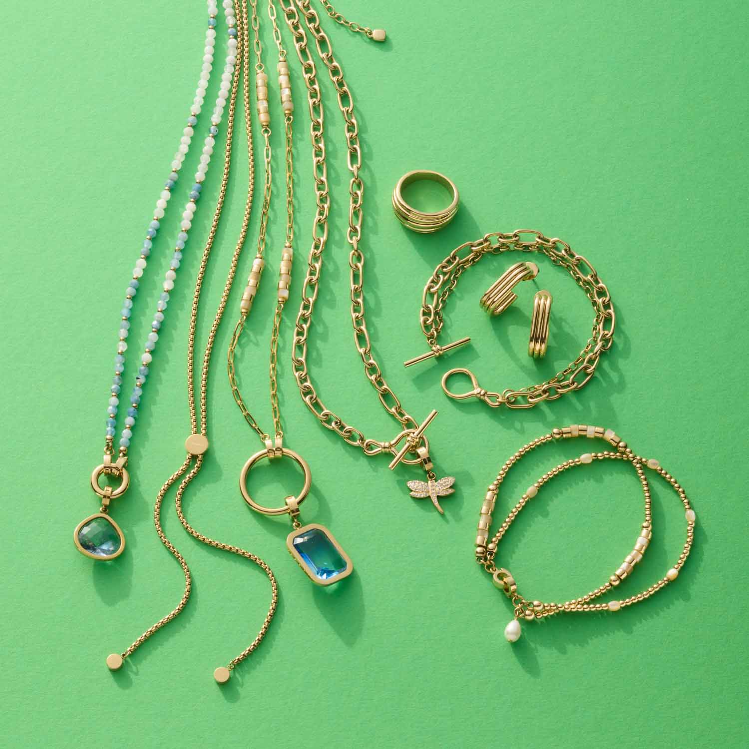 Schmuckkollektion mit goldenen Ketten, Armbändern, Ring und Ohrringen auf grünem Hintergrund