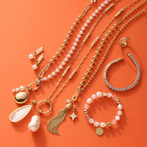 Halskette CARONNA gold mit Clip & Mix Anhängern und Armbändern auf orangefarbenem Hintergrund