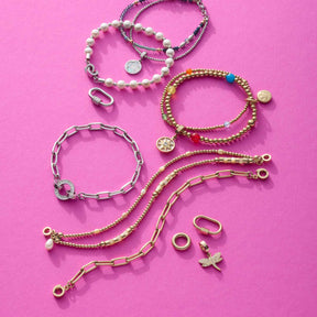 Mehrere Armbänder der Serie CLIP&MIX in Gold- und Silbertönen auf rosa Hintergrund