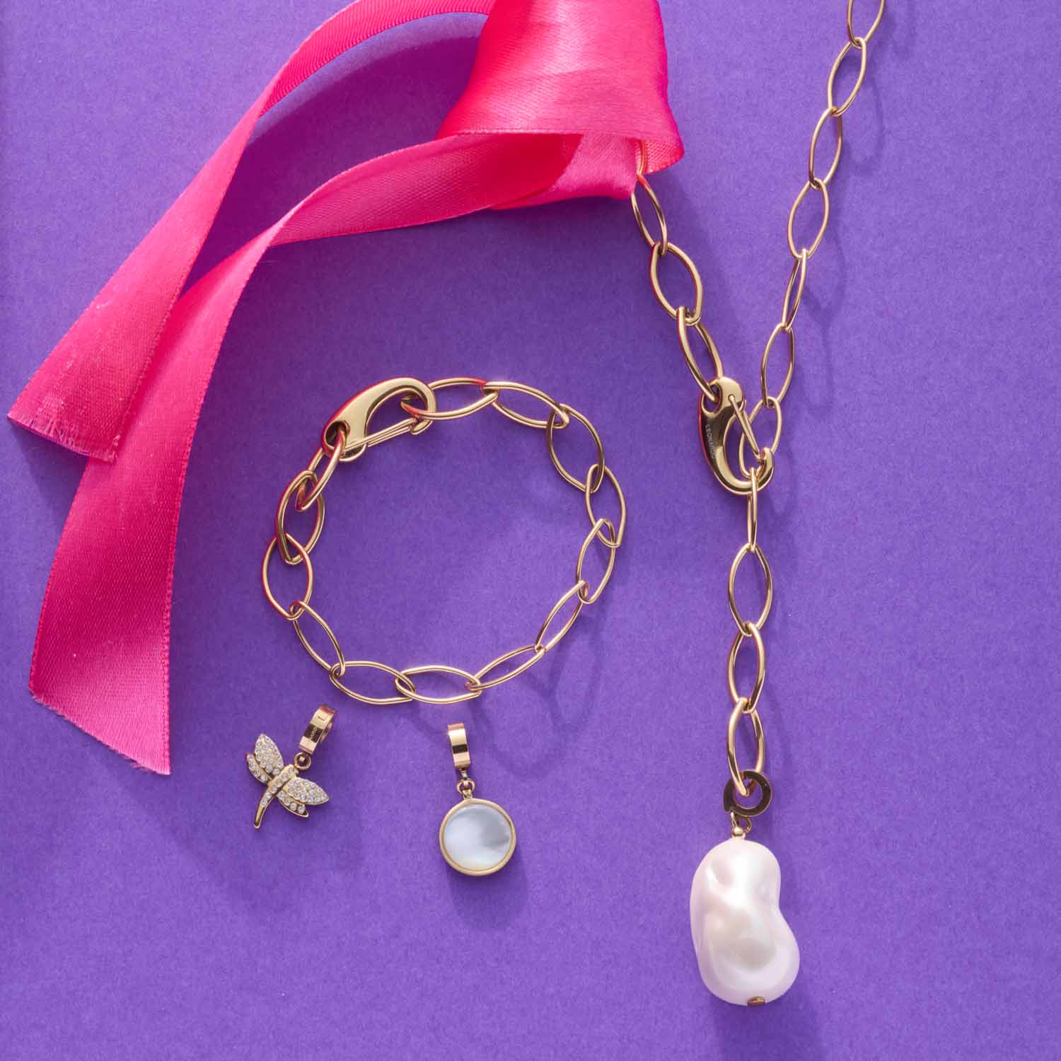Halskette TORY 80 cm gold mit Perlenanhängern auf violettem Hintergrund und pinkem Band