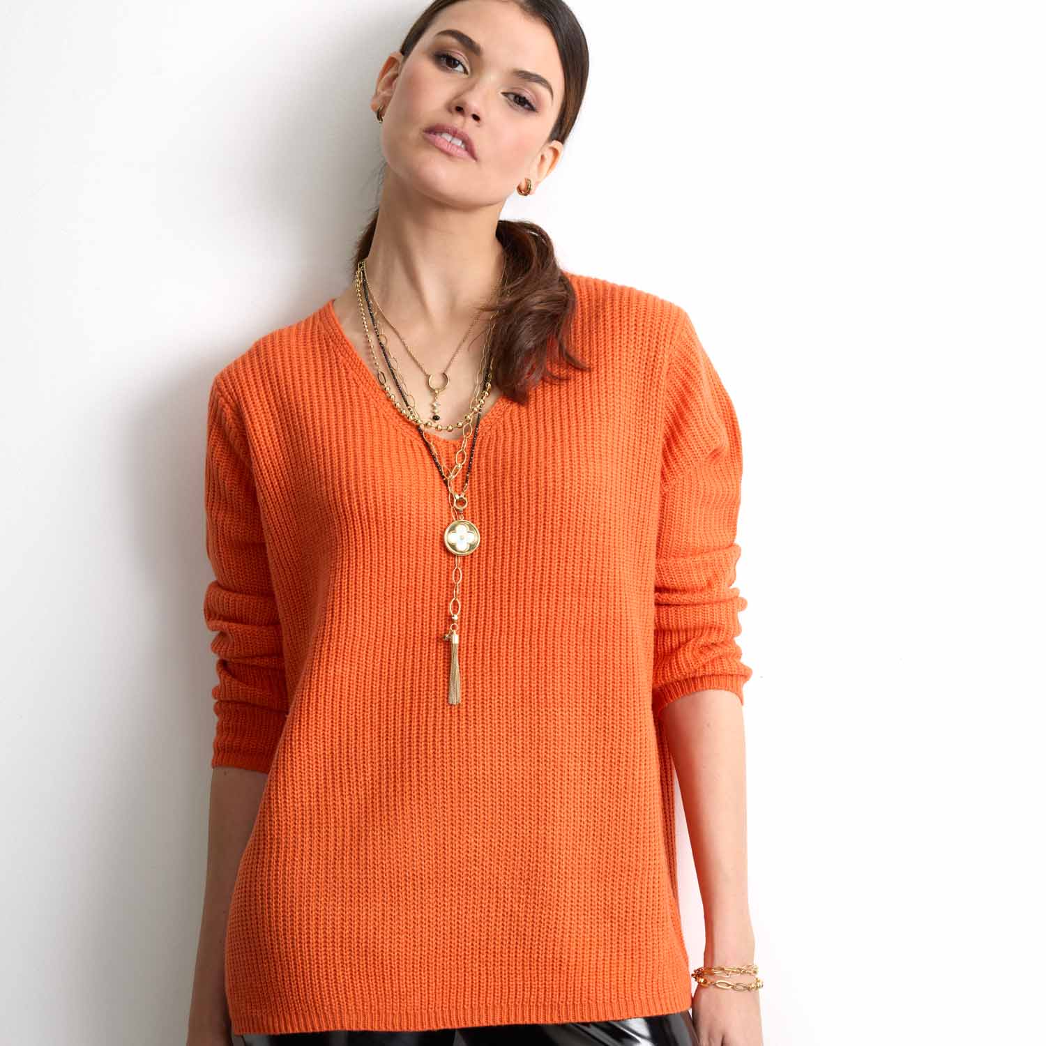 Frau trägt oranges Rippenstrick-Shirt und goldenes Armband TORY
