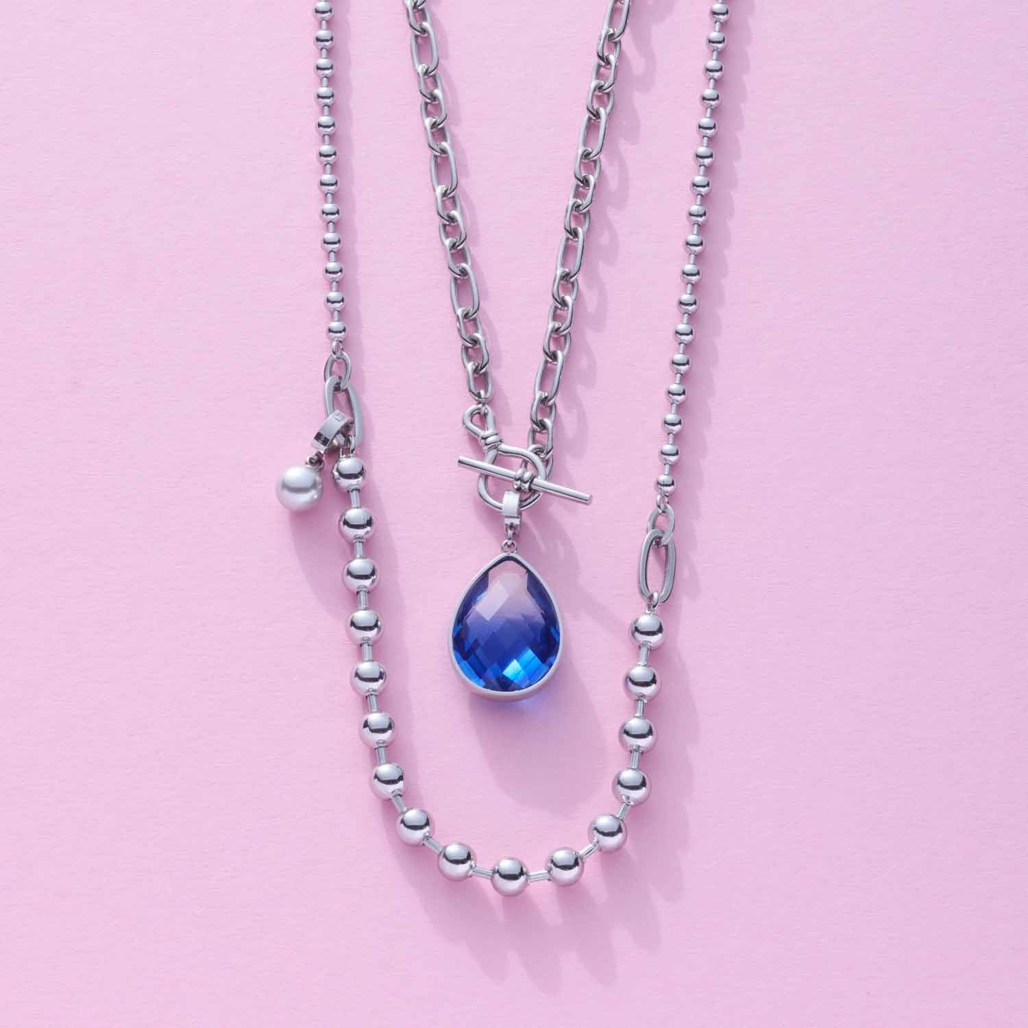 Halskette DOTTY mit silbernen Kugelgliedern und blauem Tropfenanhänger auf rosa Hintergrund