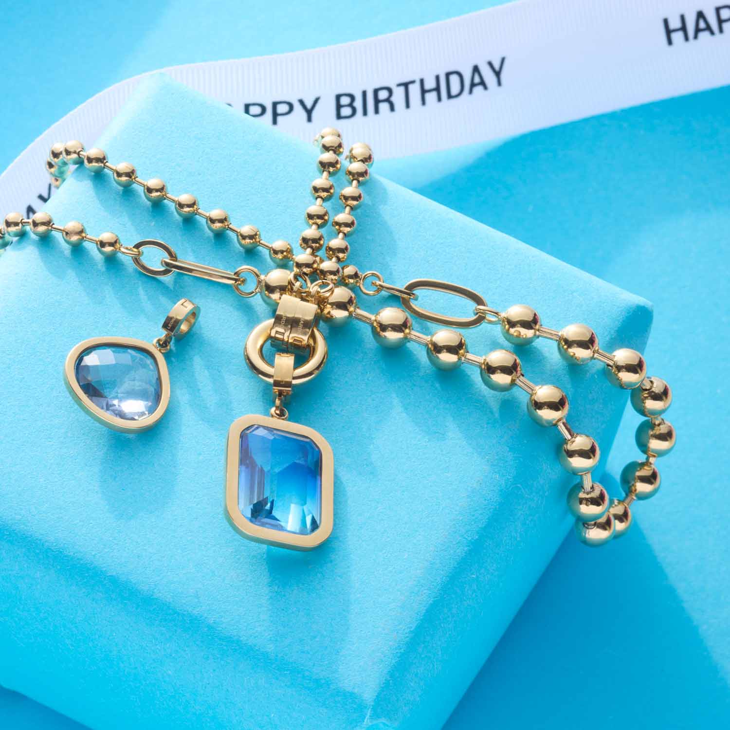 Halskette DOTTY gold mit blauen Clip-Anhängern auf blauem Geschenkkarton