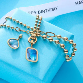 Halskette DOTTY gold mit blauen Clip-Anhängern auf blauem Geschenkkarton