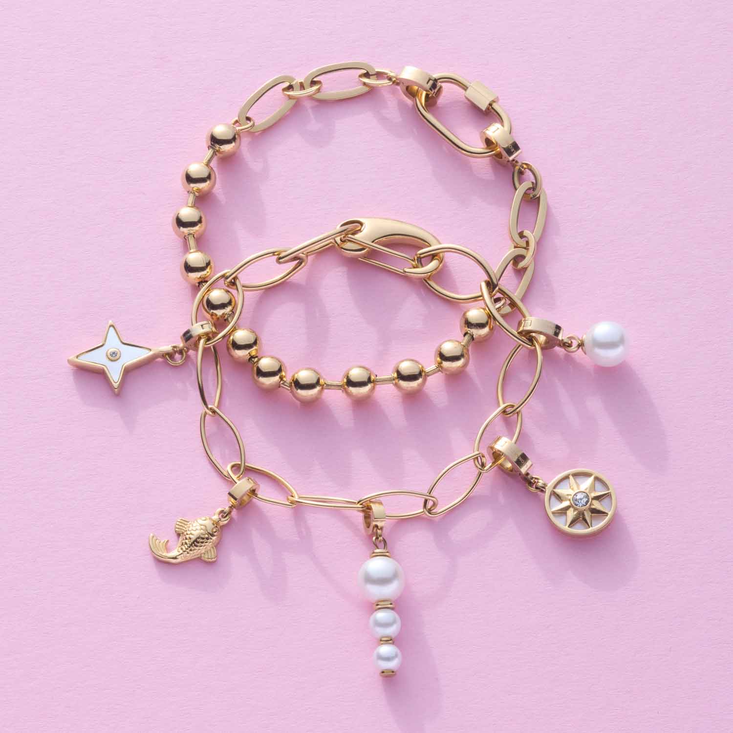 Drei goldene Armbänder DOTTY mit Perlen und Charms auf rosa Hintergrund