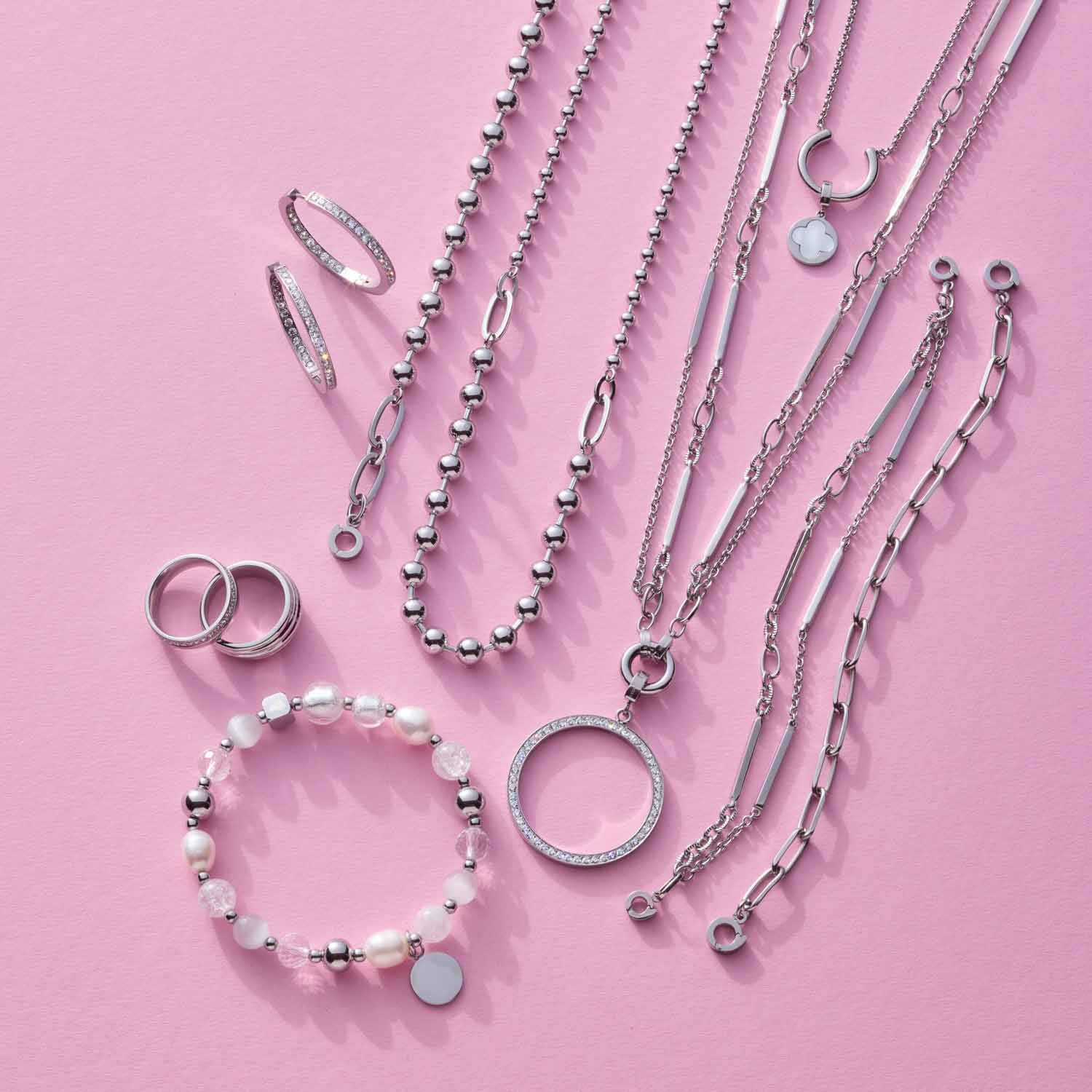 Silberne Schmuckkollection mit Halsketten, Armbändern und Ringen auf rosa Hintergrund