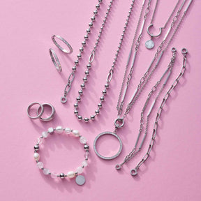 Silberne Schmuckkollection mit Halsketten, Armbändern und Ringen auf rosa Hintergrund