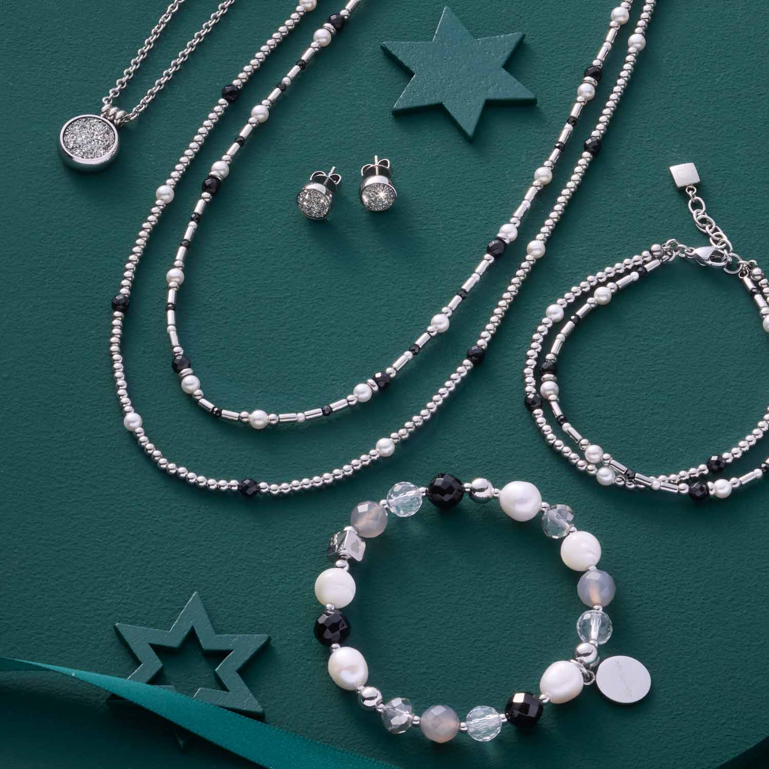 Armband SABINE mit Perlmuttkugeln, Glasperlen und schwarzen Akzenten auf grünem Untergrund neben Halsketten und Ohrringen
