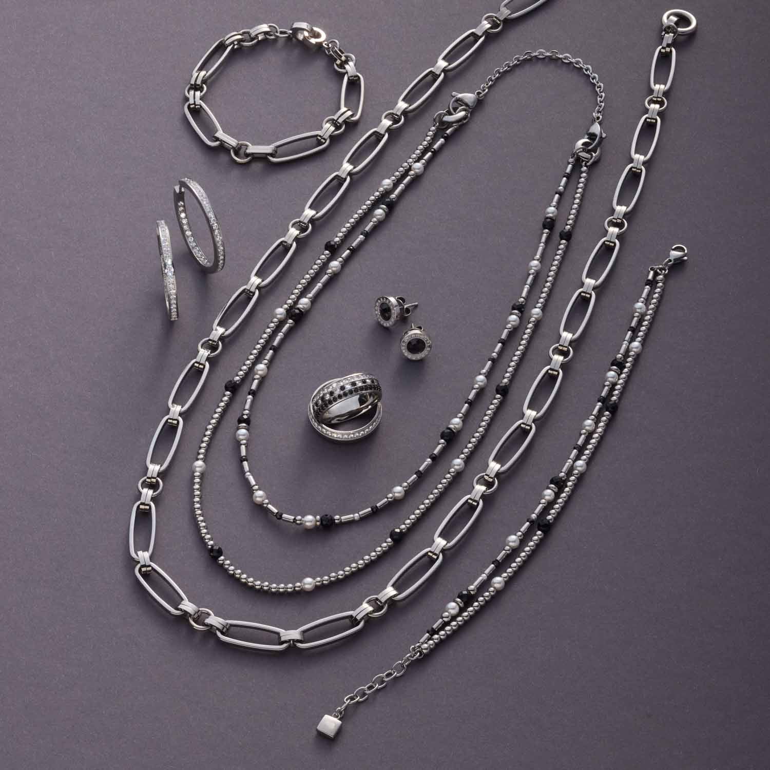 Schmuckkollektion aus Silber mit Ketten, Armband, Ring und Ohrringen auf grauem Untergrund