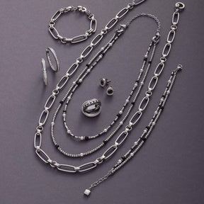 Schmuckkollektion aus Silber mit Ketten, Armband, Ring und Ohrringen auf grauem Untergrund