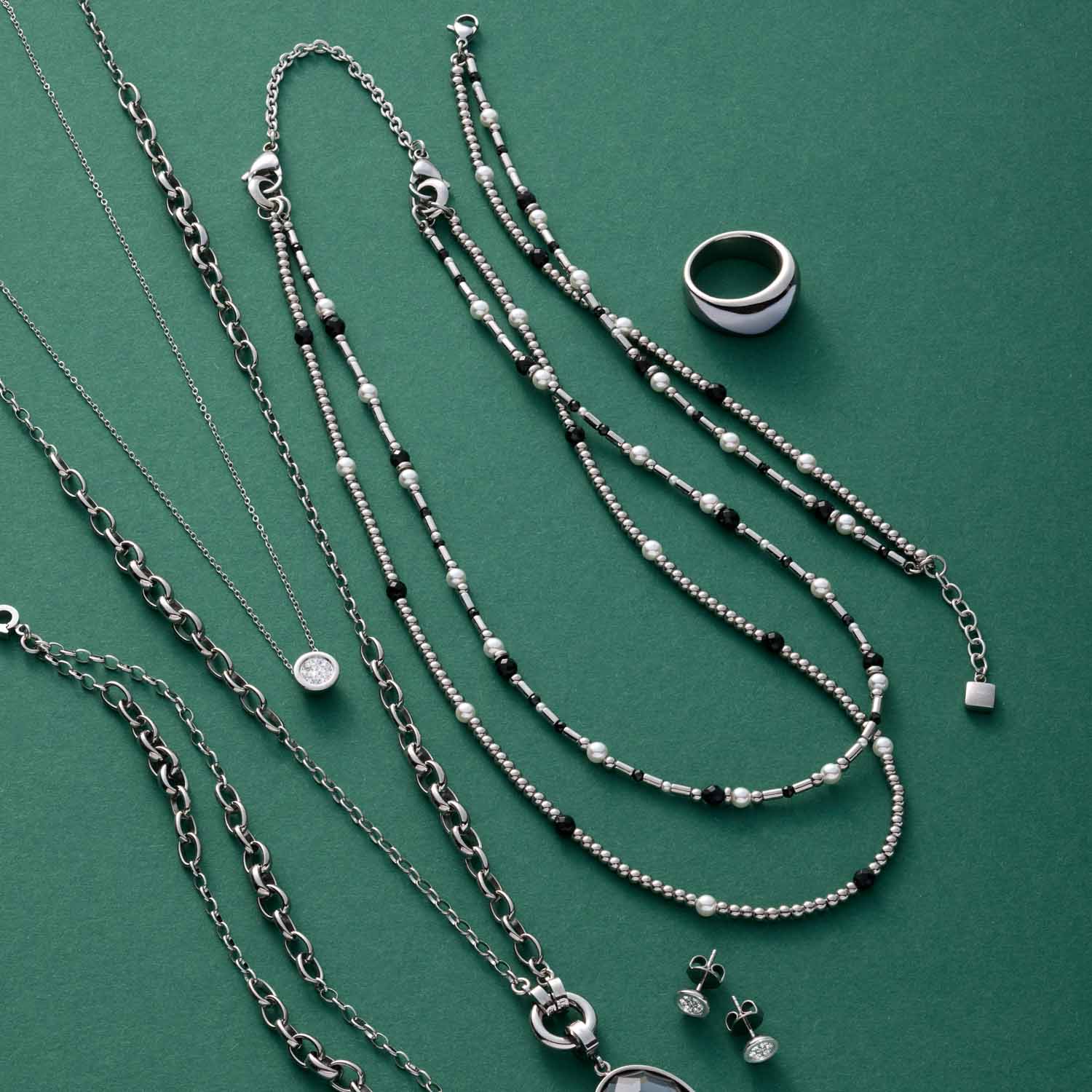Schmuckkollektion auf grünem Untergrund: Halsketten, Armbänder, Ring und Ohrstecker aus Silber und Glas