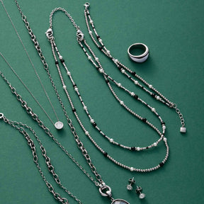 Schmuckkollektion auf grünem Untergrund: Halsketten, Armbänder, Ring und Ohrstecker aus Silber und Glas