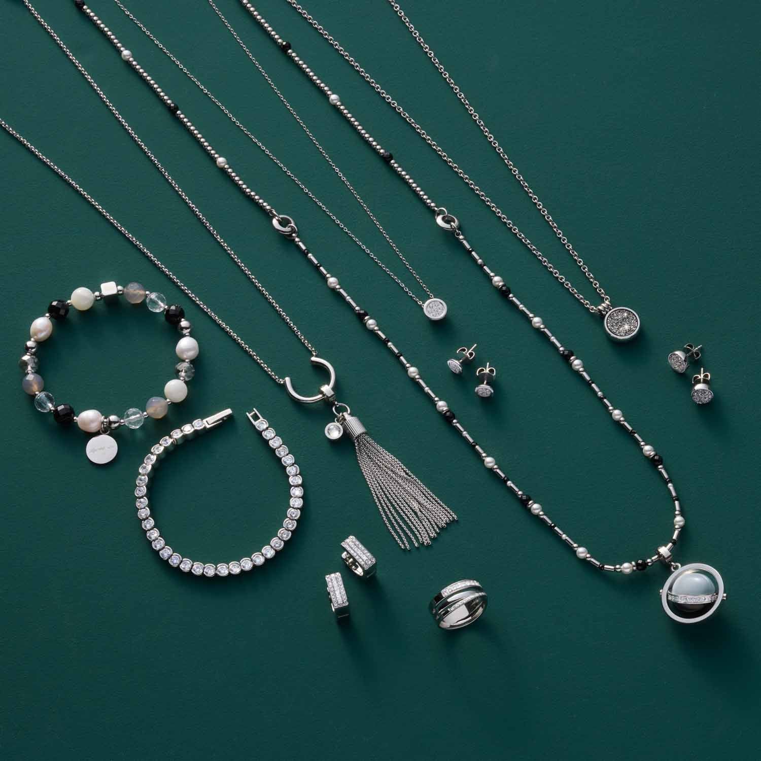 Schmuckkollektion auf grünem Hintergrund mit Halsketten, Armbändern, Ringen und Ohrringen aus Edelstahl