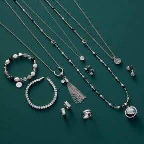 Schmuckkollektion auf grünem Hintergrund mit Halsketten, Armbändern, Ringen und Ohrringen aus Edelstahl