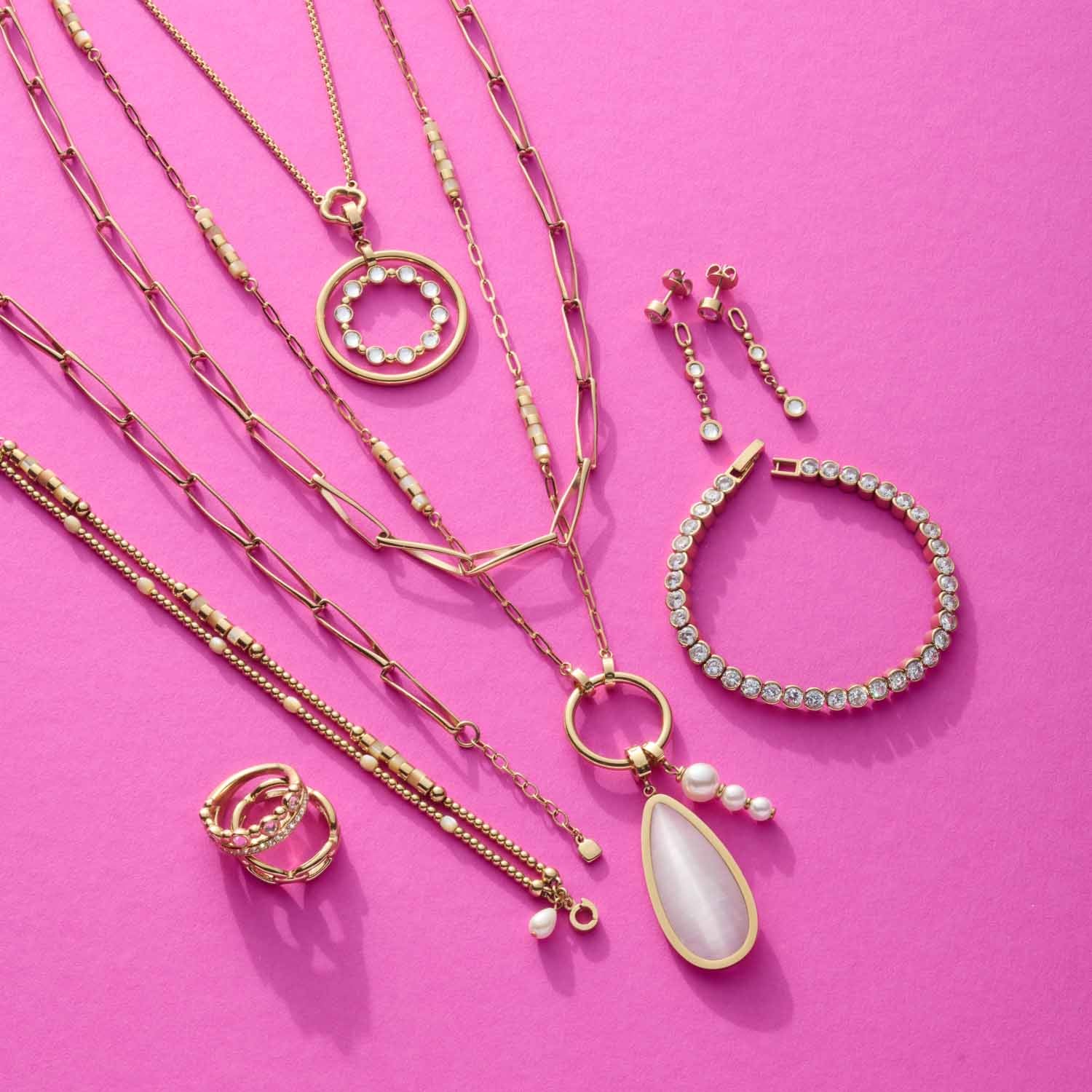 Goldene Schmuckkollektion mit Halsketten, Armband und Ohrringen auf rosa Hintergrund