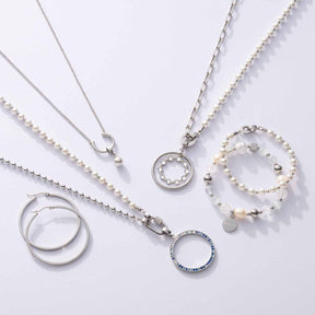Schmuckkollektion mit Anhängern, Halsketten und Armbändern aus Edelstahl und Perlen auf weißem Hintergrund