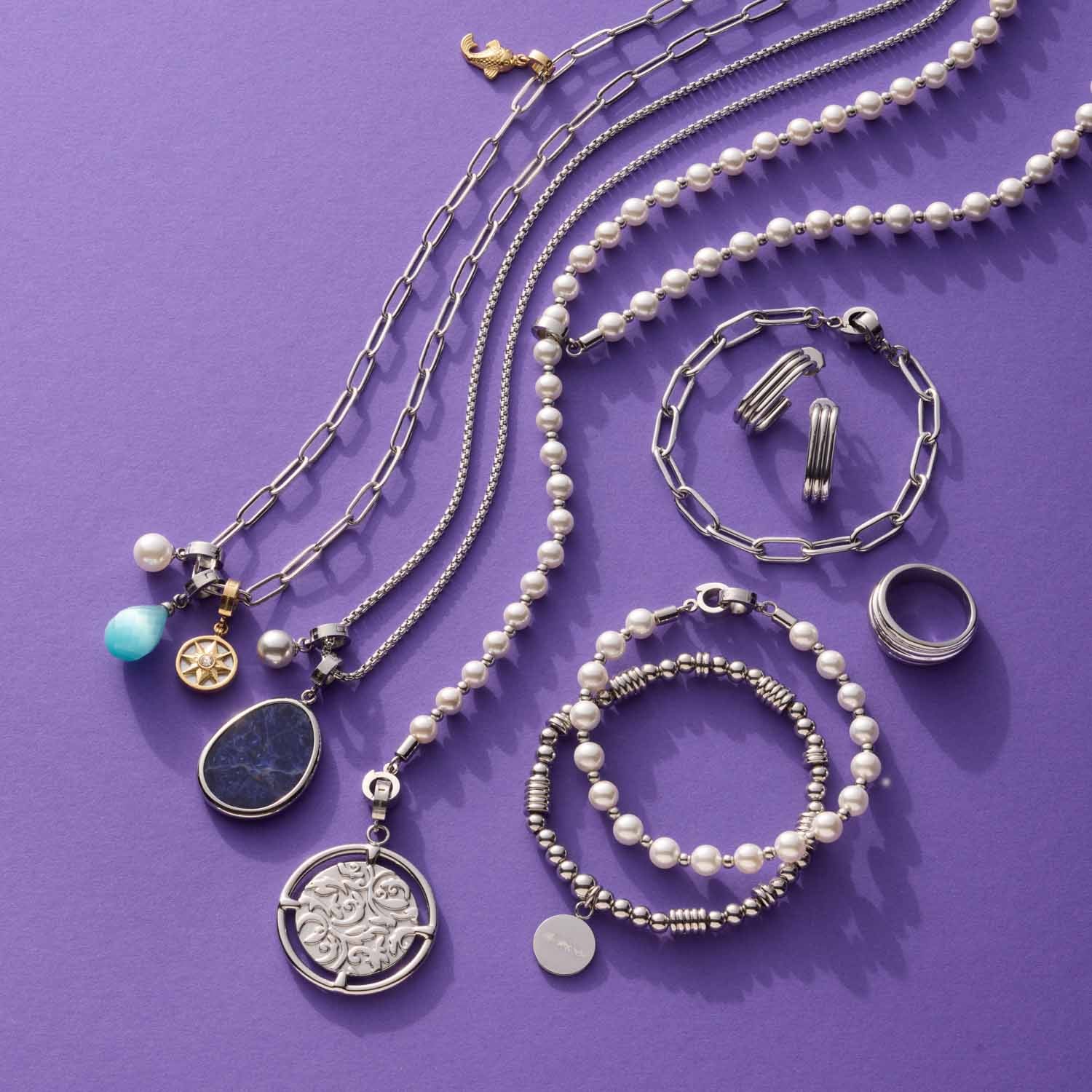 Silberne Schmuckkollektion auf violettem Hintergrund: Ketten, Armbänder, Anhänger TERRY Clip & Mix, Ringe und Ohrringe