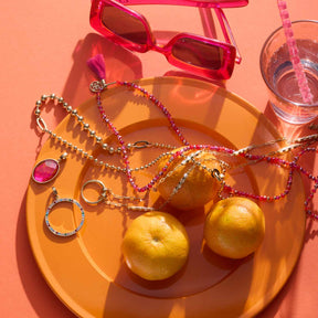 Anhänger CLARENCE gold Clip & Mix mit Schmuck und Früchten auf orangefarbenem Tablett
