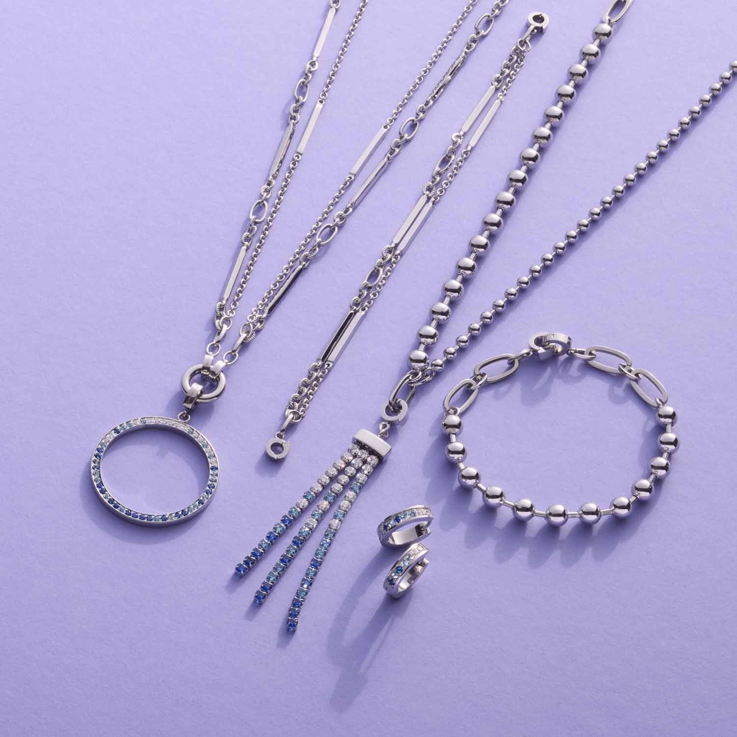 Silberne Schmuckkollektion mit Halsketten, Armband und Ringen auf violettem Hintergrund