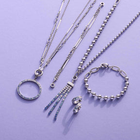 Silberne Schmuckkollektion mit Halsketten, Armband und Ringen auf violettem Hintergrund