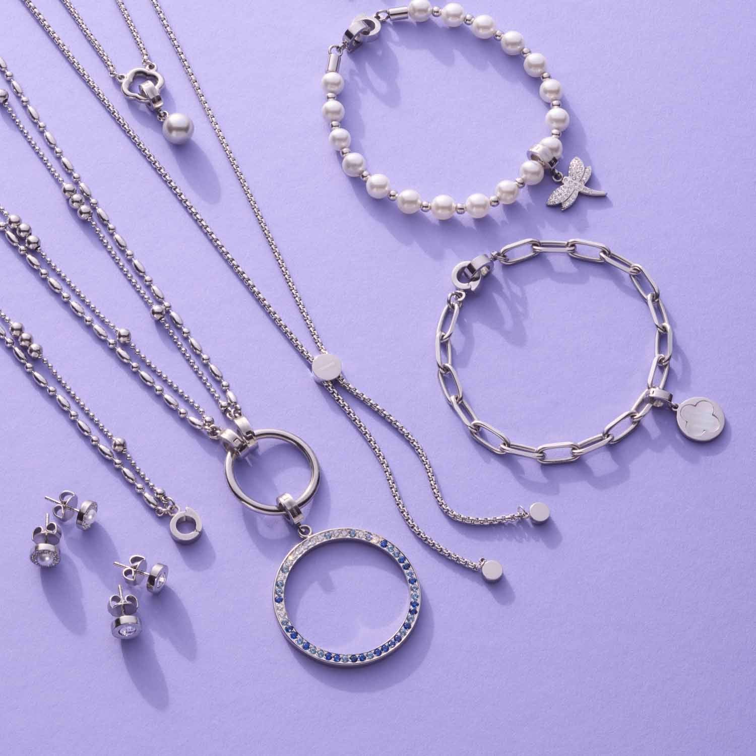 Silberner Schmuck auf violettem Hintergrund: Halsketten, Armbänder, Ohrringe und Ringe mit Glasperlen und Metallanhängern