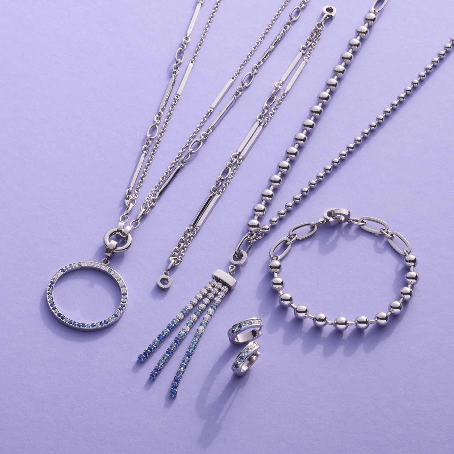 Silberne Schmuckkollektion mit Halsketten, Anhängern, Armband und Ohrringen auf violettem Hintergrund