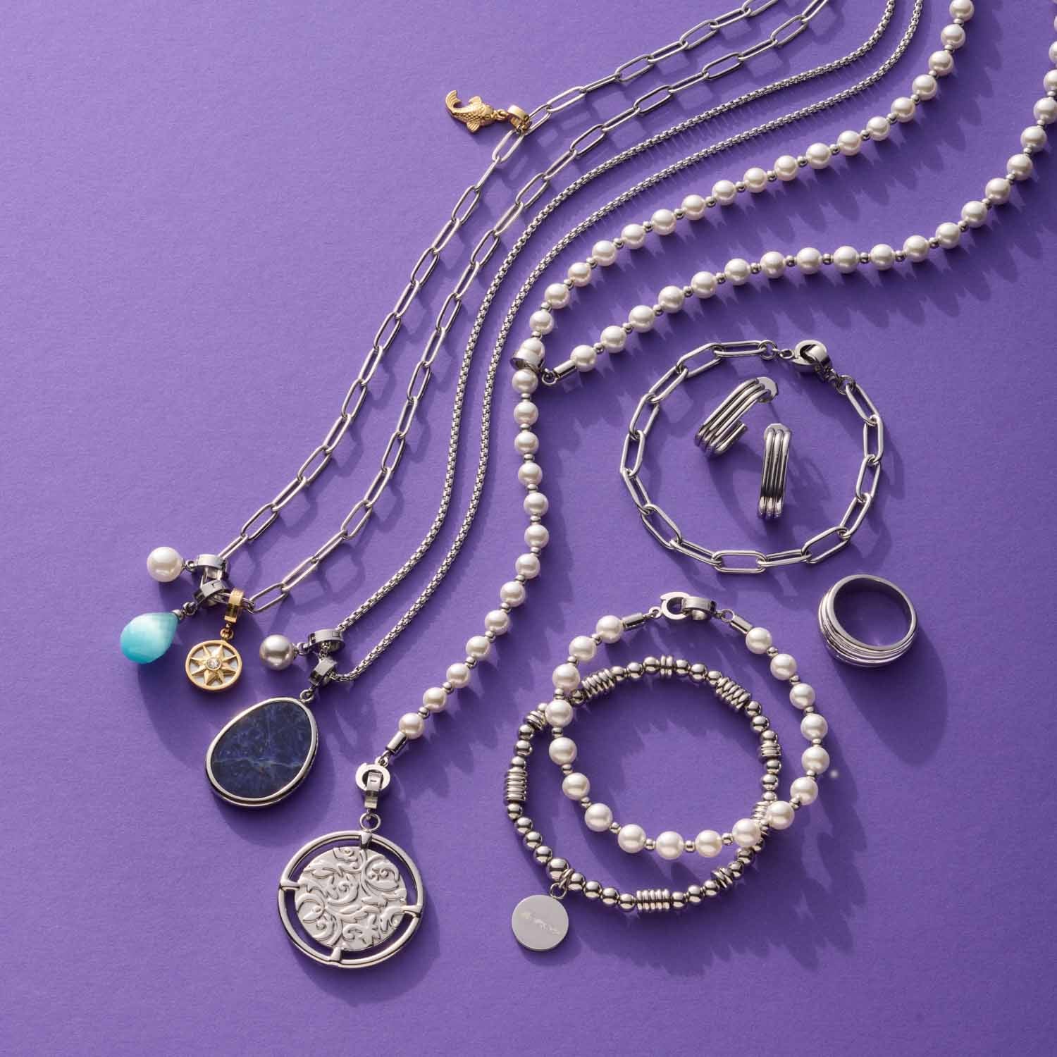 Schmuckkollektion mit Anhängern, Ketten, Armbändern und Ringen auf violettem Hintergrund