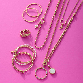 Goldener Schmuck auf rosa Hintergrund, Ketten, Ringe und Anhänger arrangiert