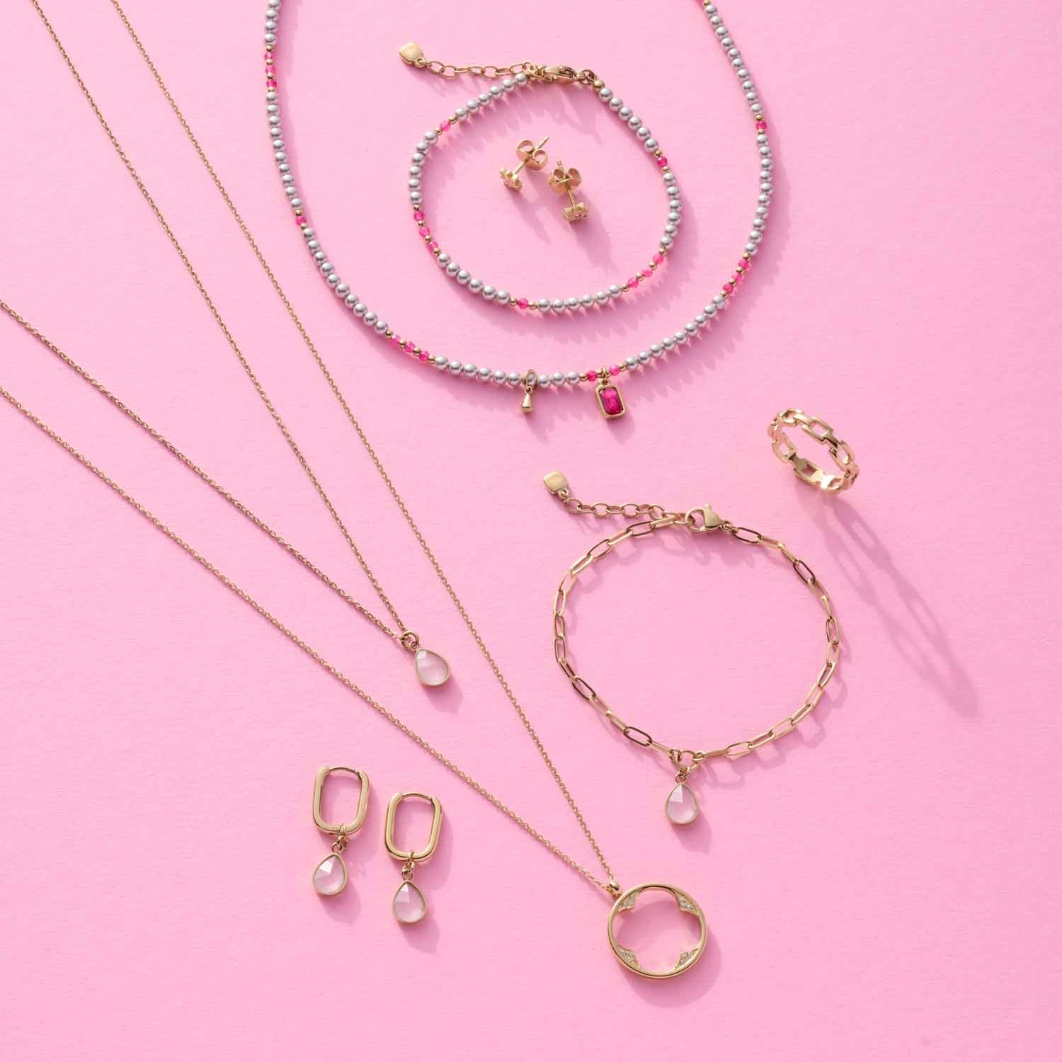 Schmuckkollektion mit Armbändern, Ketten, Ohrringen und Ring in Gold und Pastelltönen auf rosa Hintergrund