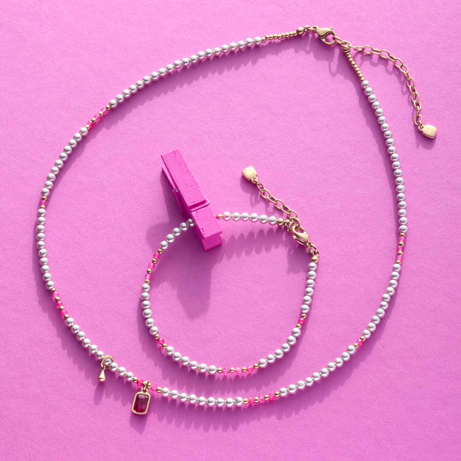 Halskette PINKY 42 cm gold CIAO mit Glasperlen auf rosa Hintergrund, daneben pink farbener Schmuckständer