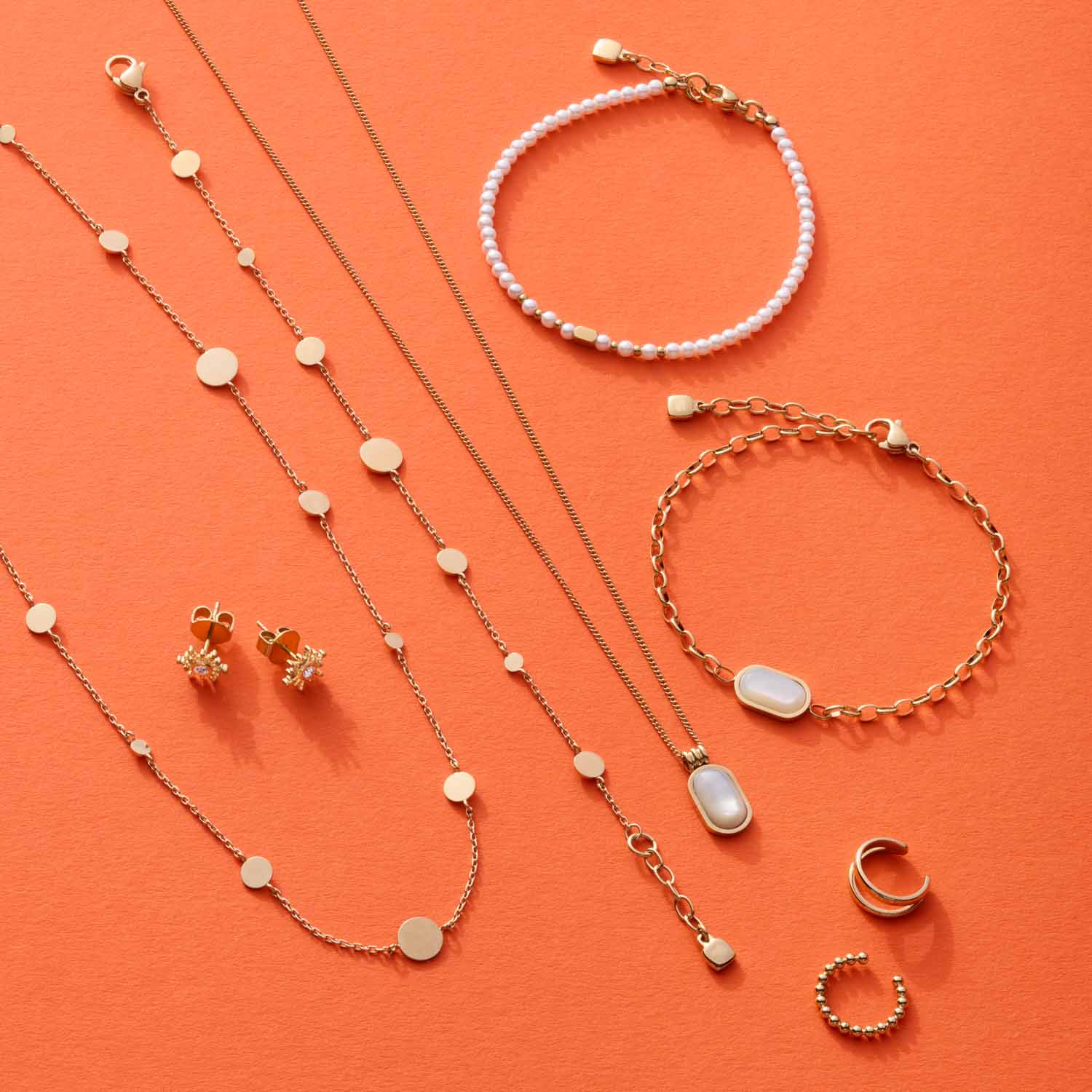Schmuckkollektion auf orangefarbenem Hintergrund: Halsketten, Armbänder und Ohrringe aus Edelstahl mit Perlmutt
