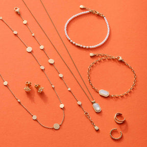 Schmuckkollektion auf orangefarbenem Hintergrund: Halsketten, Armbänder und Ohrringe aus Edelstahl mit Perlmutt