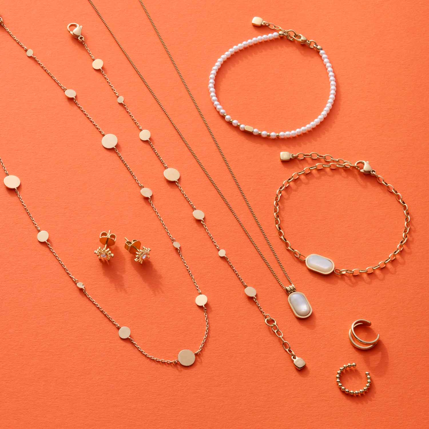 Schmuckkollektion mit Armbändern, Ketten und Ohrringen in Gold und Perlmutt auf orangefarbenem Hintergrund