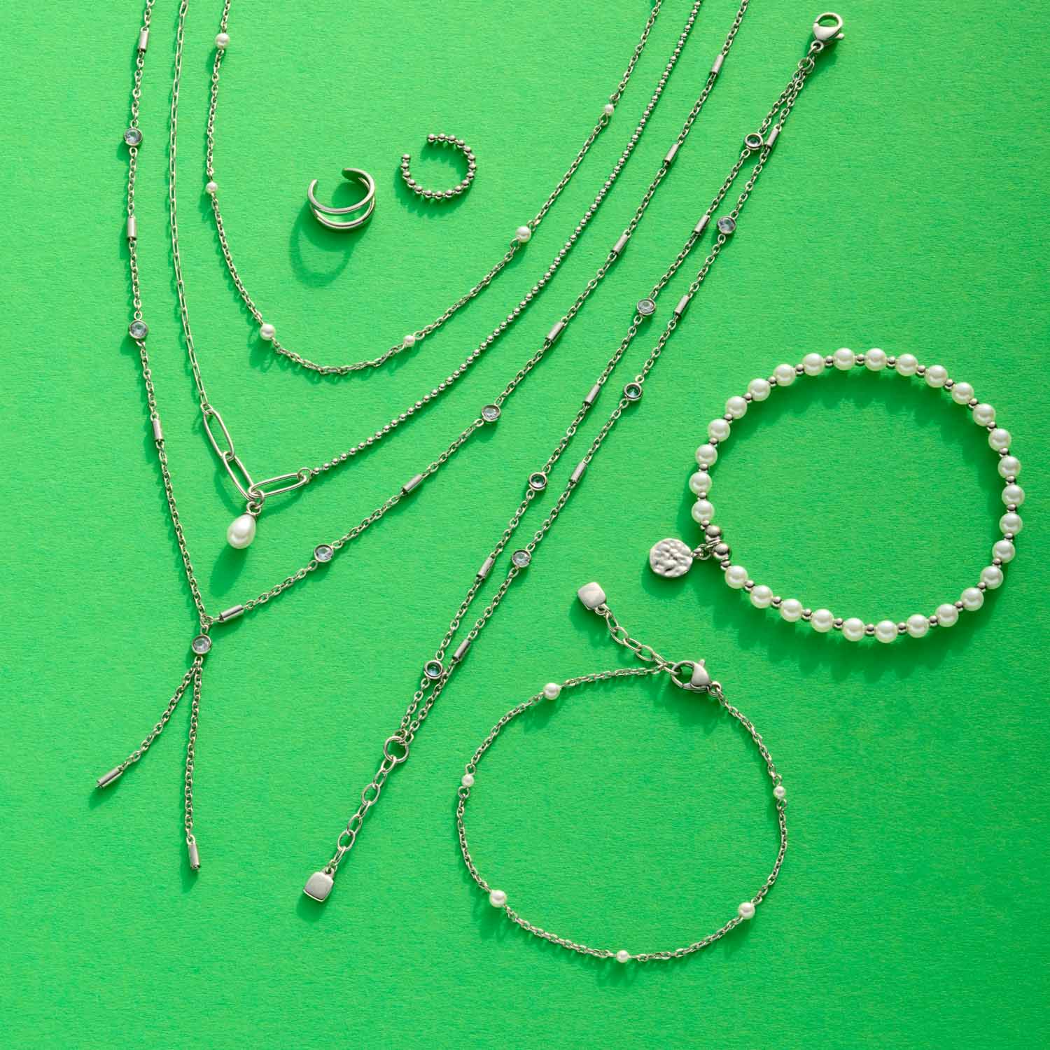 Silberne Halsketten und Armbänder mit Glasperlen auf grünem Hintergrund