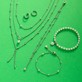 Silberne Schmuckkollektion auf grünem Hintergrund mit Armbändern, Ringen und Halsketten aus Glas