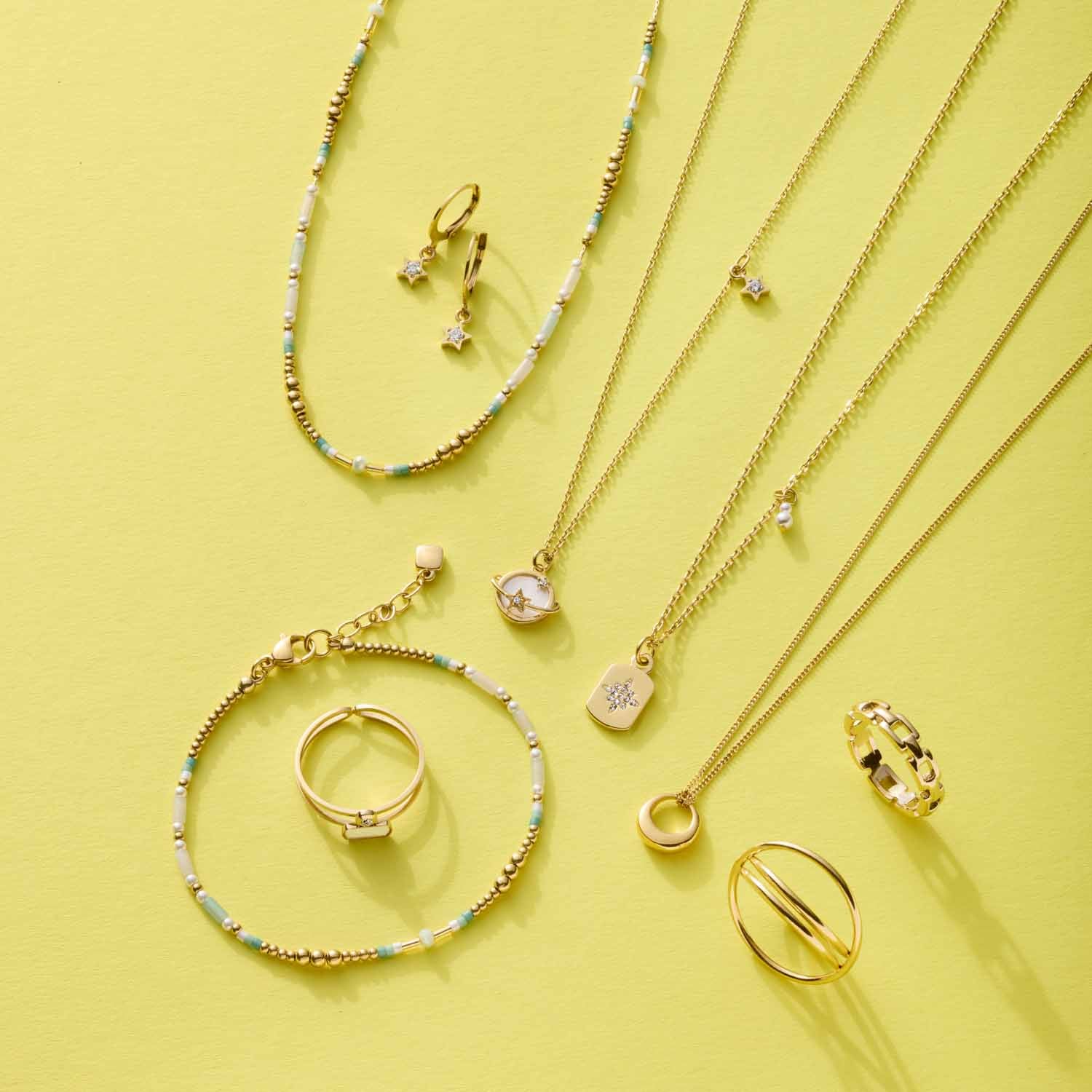 Goldene Halsketten, Ringe und Armbänder auf gelbem Hintergrund arrangiert