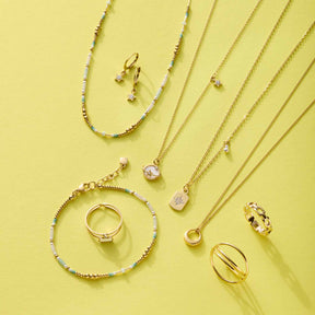 Armband LILLY gold CIAO mit Glas-Perlen auf gelbem Hintergrund, umgeben von weiteren Schmuckstücken der Serie