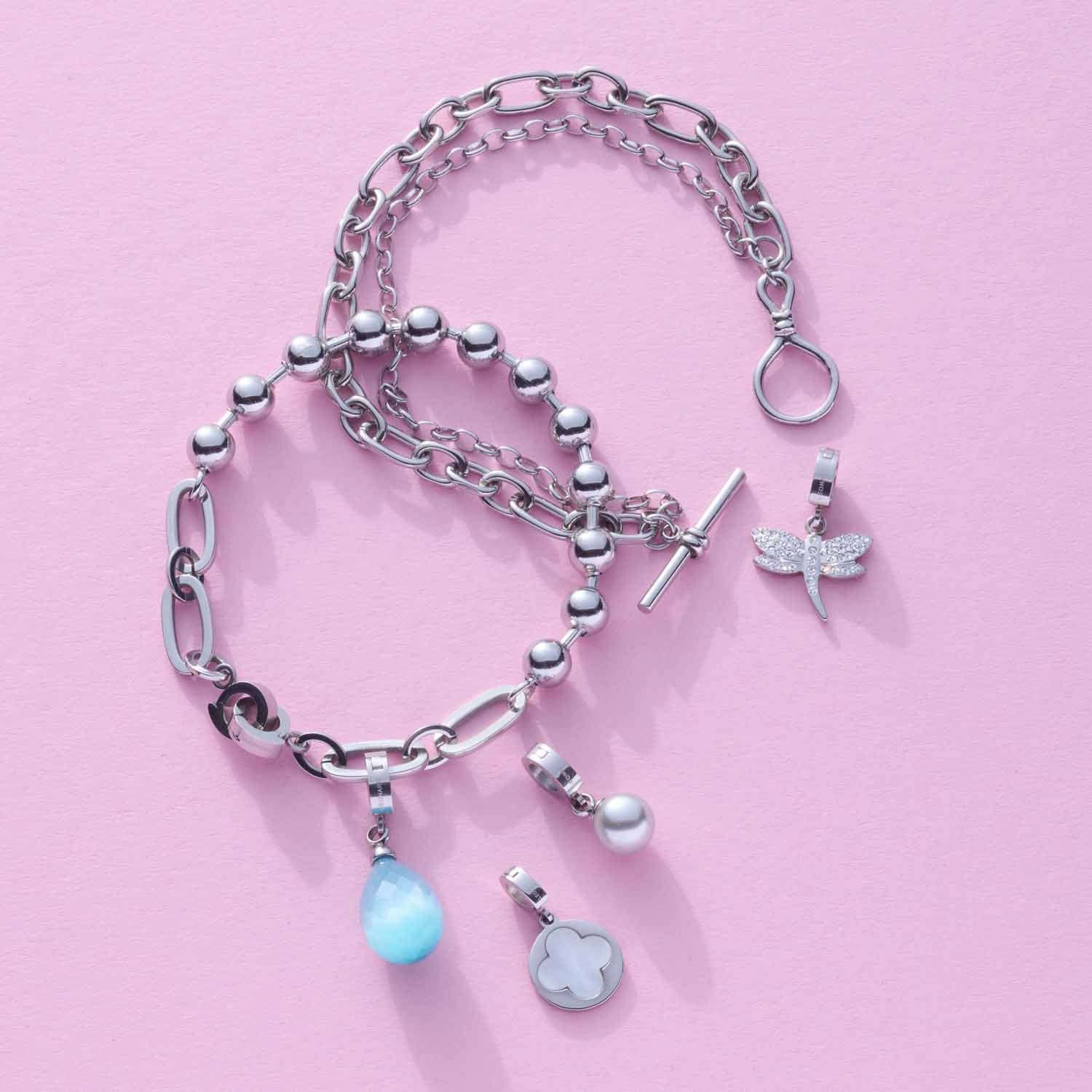 Armband ELISABETH mit Kettengliedern, Perlen und Anhängern auf rosa Hintergrund