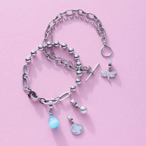 Armband ELISABETH mit Kettengliedern, Perlen und Anhängern auf rosa Hintergrund