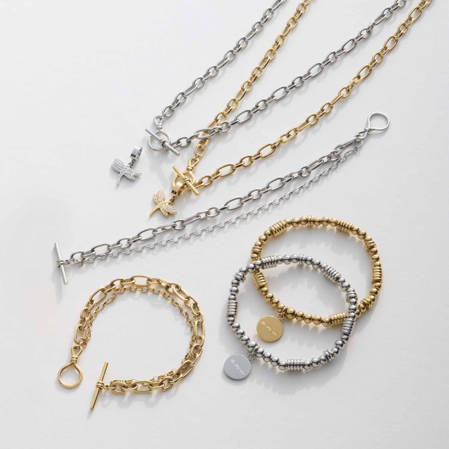 Mehrere Armbänder und Ketten in Silber und Gold auf weißem Hintergrund, teilweise mit Anhängern