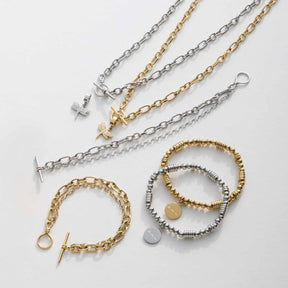 Mehrere Armbänder und Ketten in Silber und Gold auf weißem Hintergrund, teilweise mit Anhängern