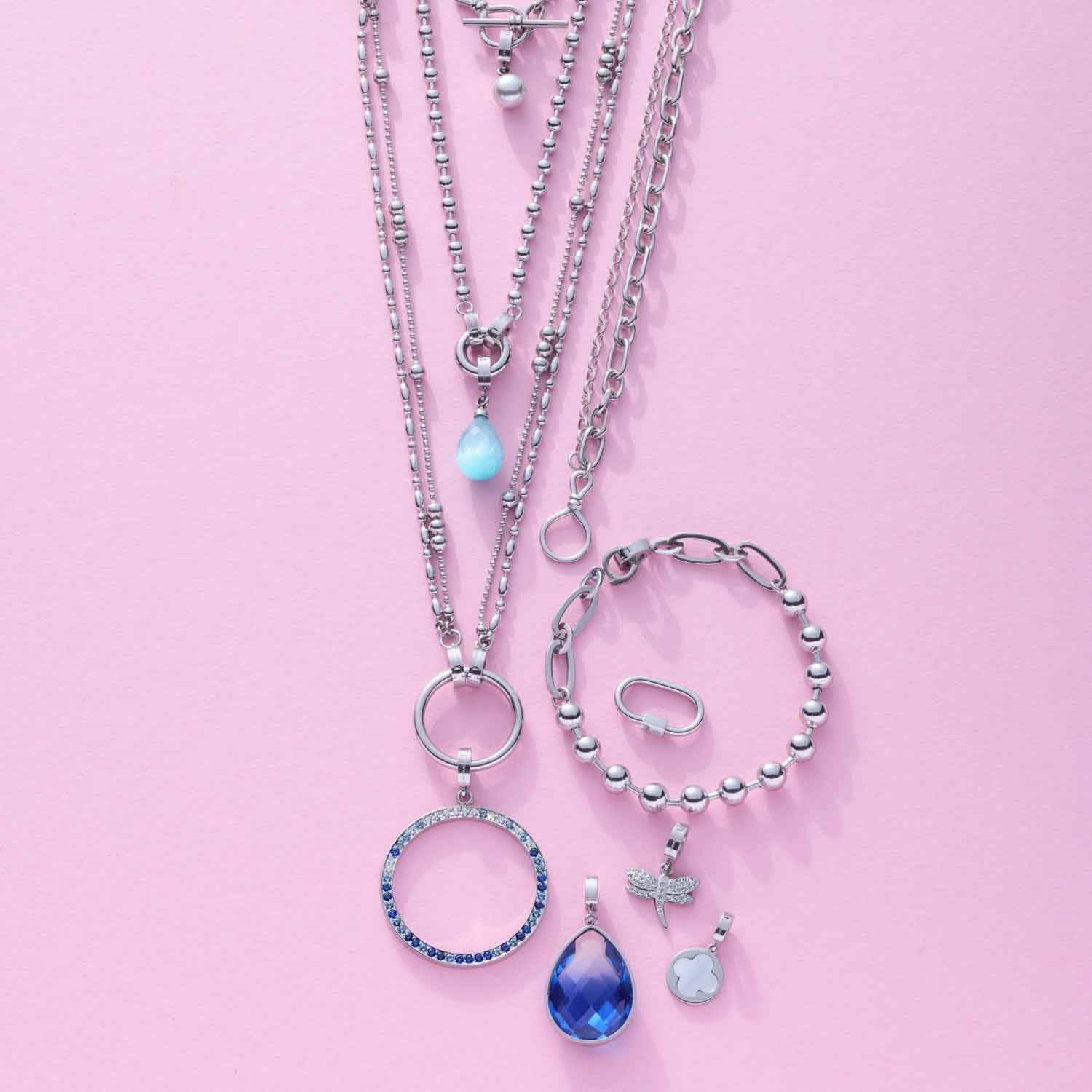 Silbernes Schmuckset mit Armbändern, Halsketten und Anhängern auf rosa Hintergrund