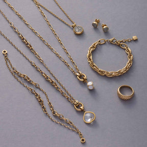 Goldene Schmuckkollektion mit Ketten, Ringen, Armband und Ohrringen auf grauem Hintergrund
