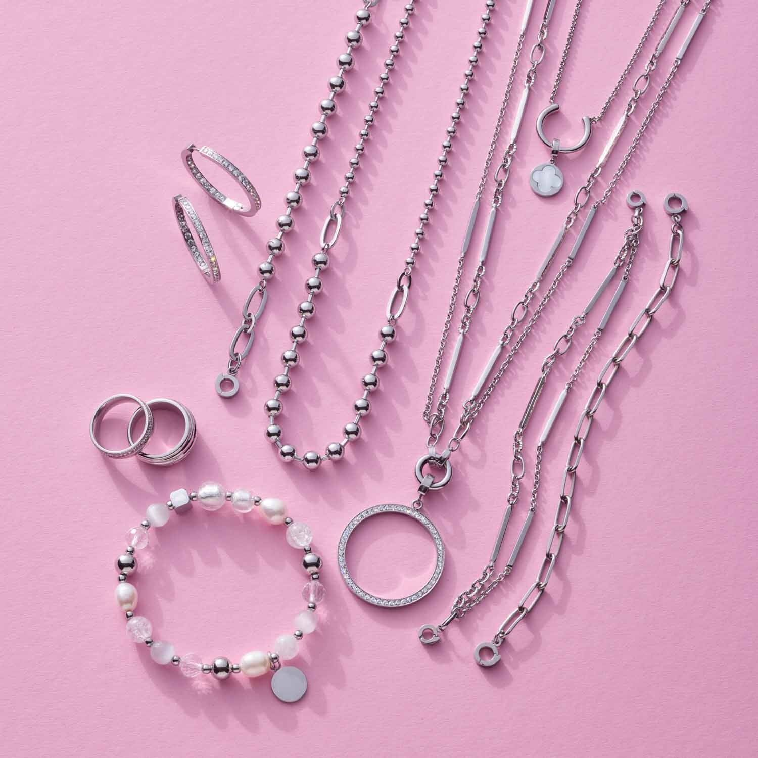 Silberner Schmuck auf rosa Hintergrund: Ringe, Ketten und Armband aus Edelstahl