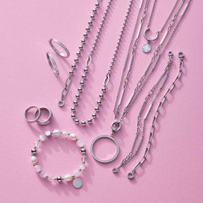 Silberne Schmuckkollektion mit Ringen, Ketten und Armband auf rosa Hintergrund