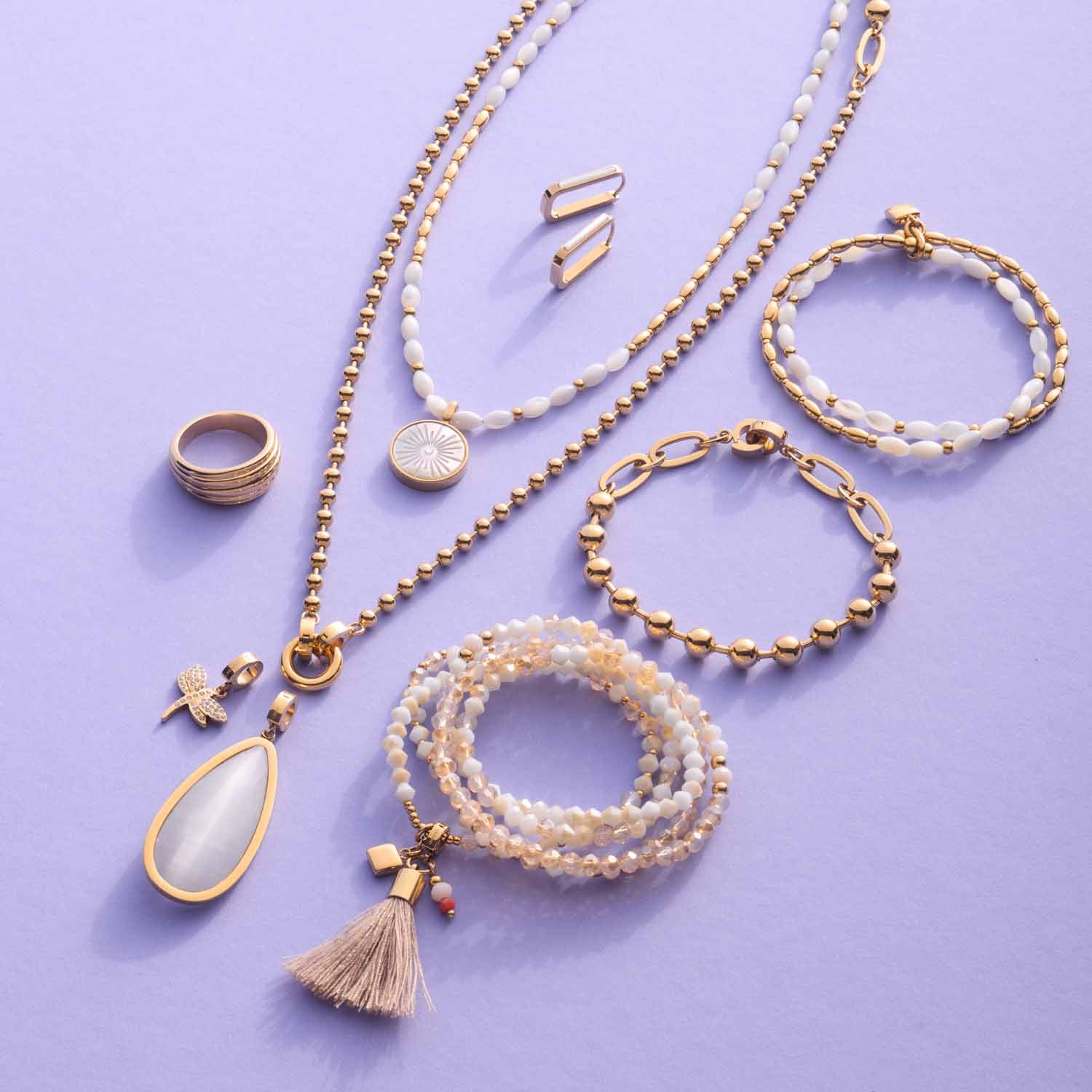 Schmuckkollektion aus gold mit Ringen, Ketten, Armbändern und Ohrringen auf violettem Hintergrund