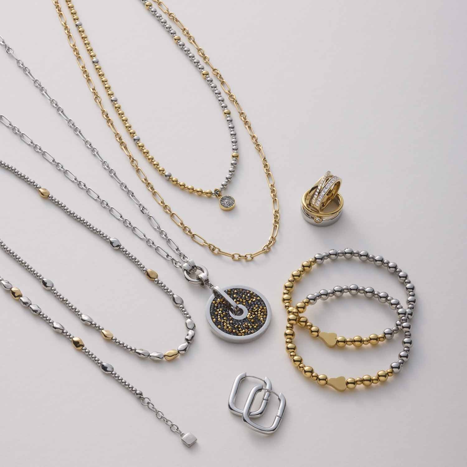 Halskette VEJA mit Anhängern, Ringen und Armbändern in Gold und Silber auf neutralem Hintergrund