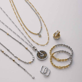 Halskette VEJA mit Anhängern, Ringen und Armbändern in Gold und Silber auf neutralem Hintergrund